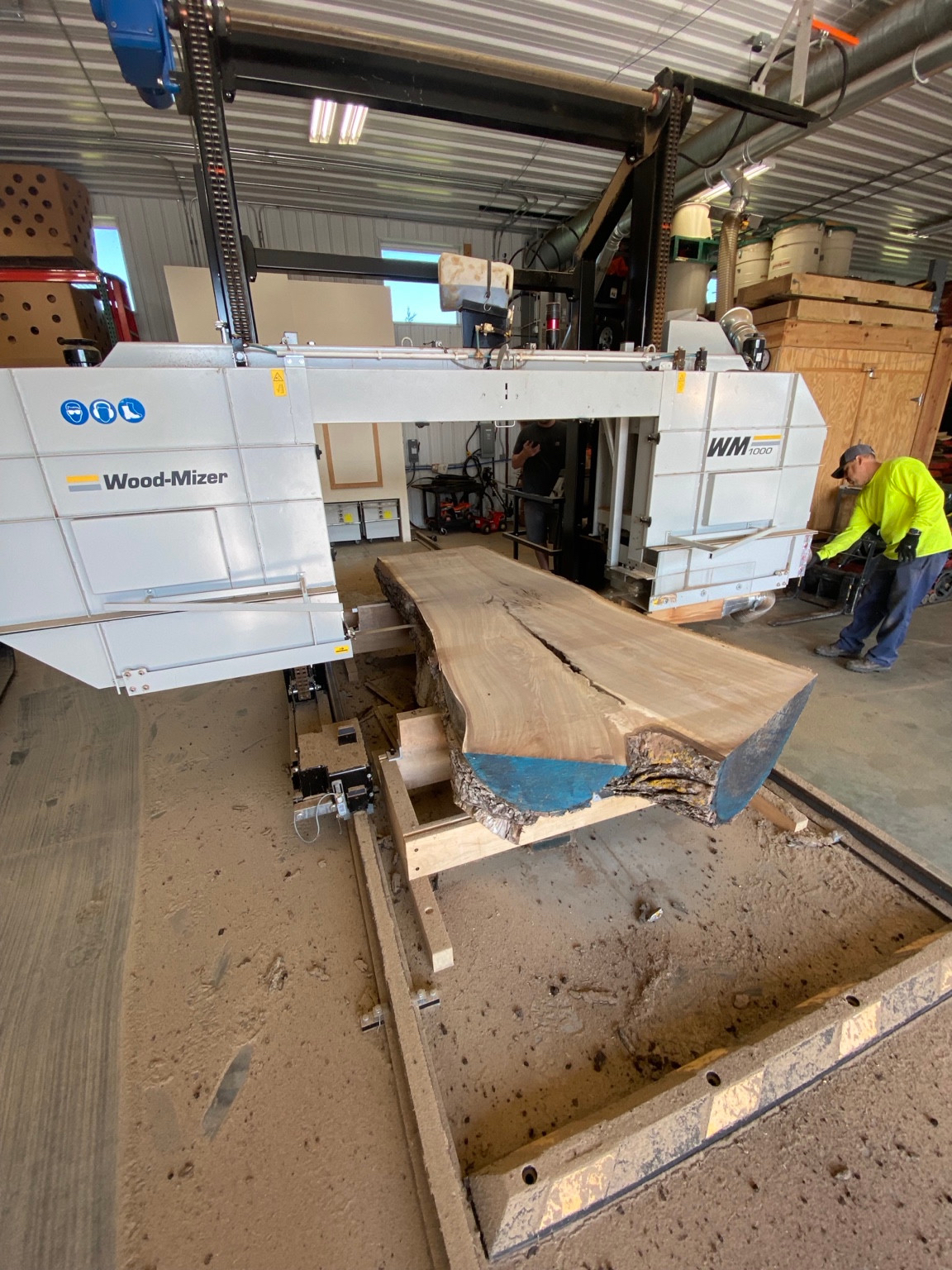 A live-edge slab on the Wood-Mizer sawmill in the Big Rock Woodworks shop, with workers beside the machine